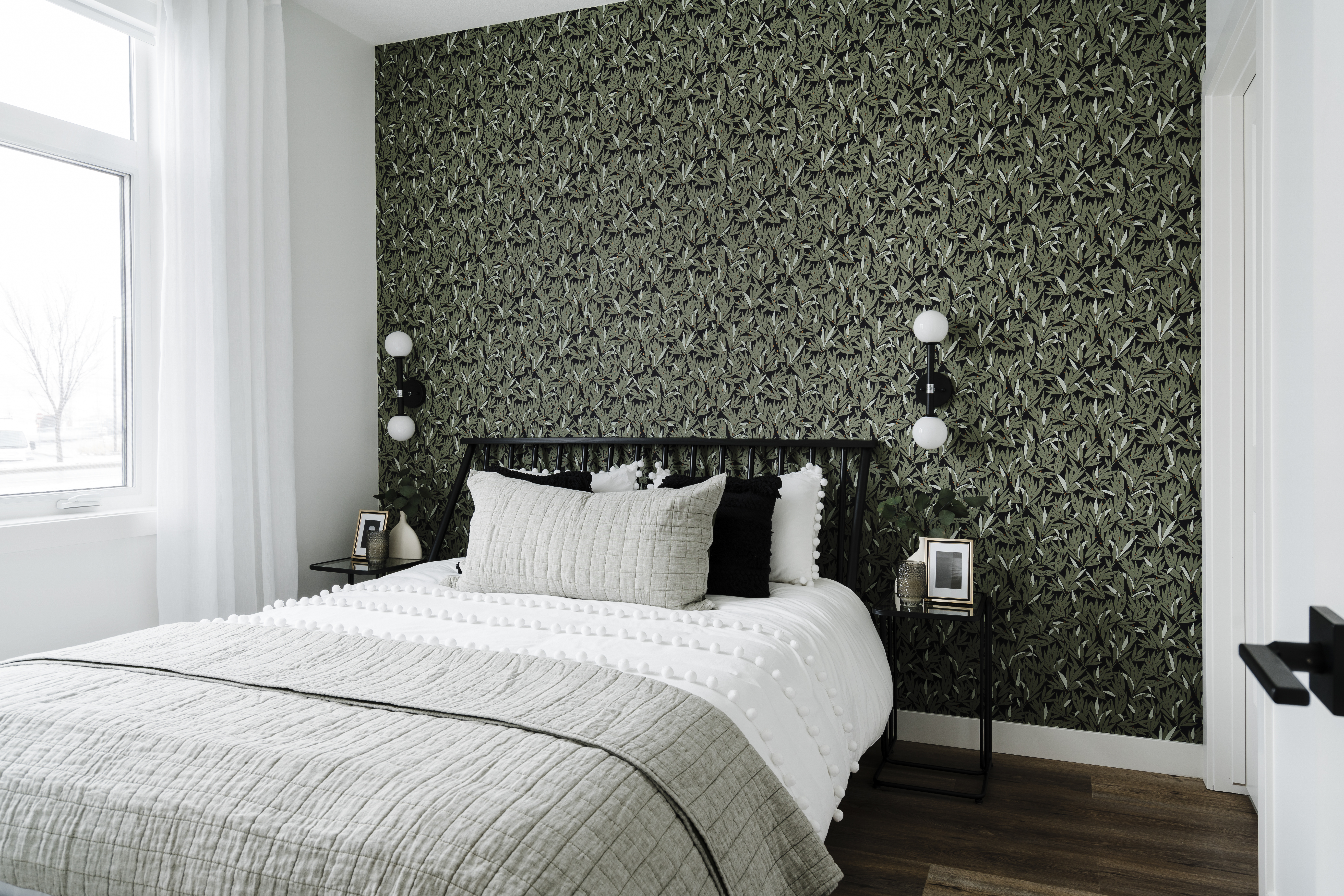 Bedroom with green patterned wallpaper, hardwood floors, and modern wall sconces.