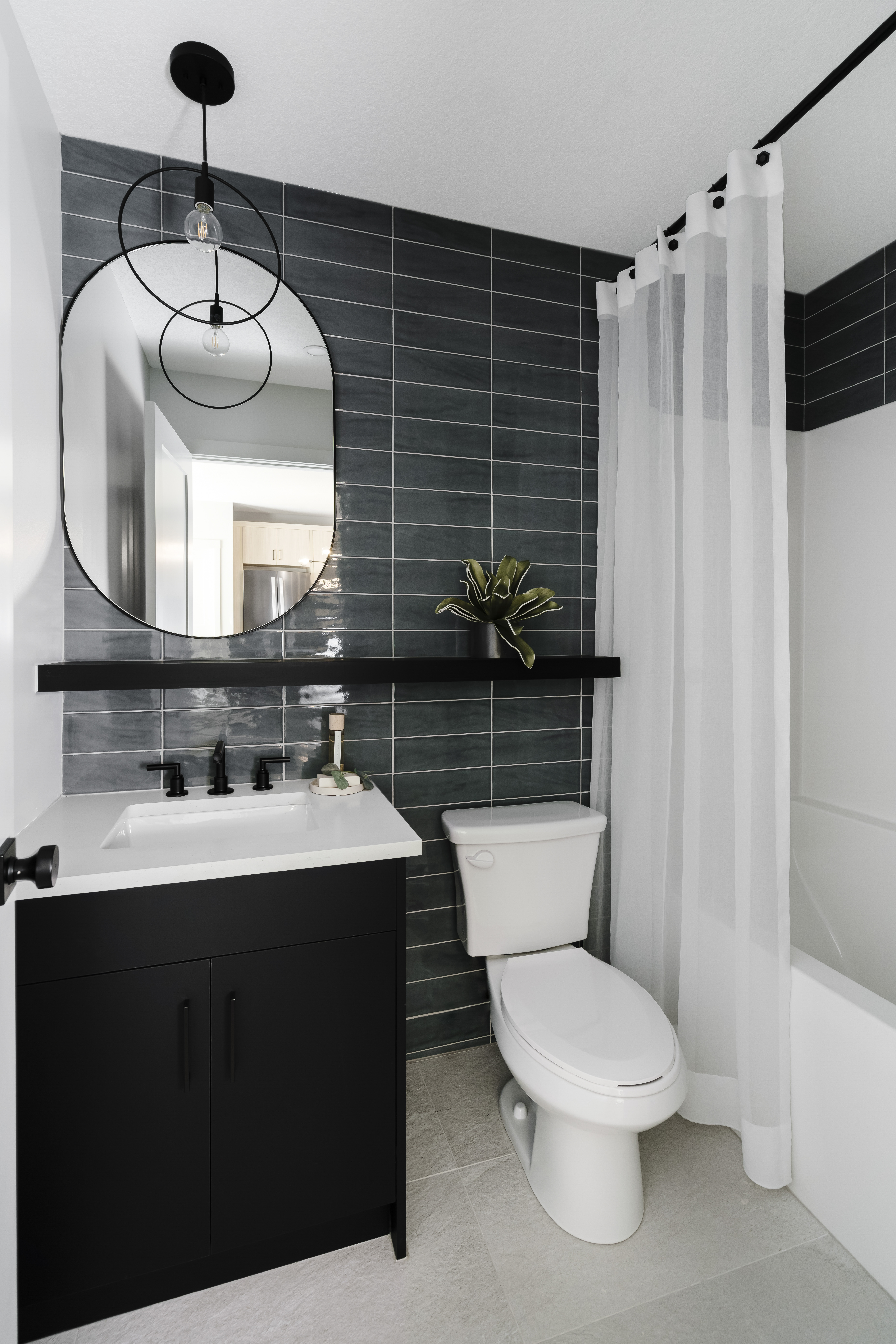 Bathroom with floating shelf and black vanity with floor to ceiling subway tile.