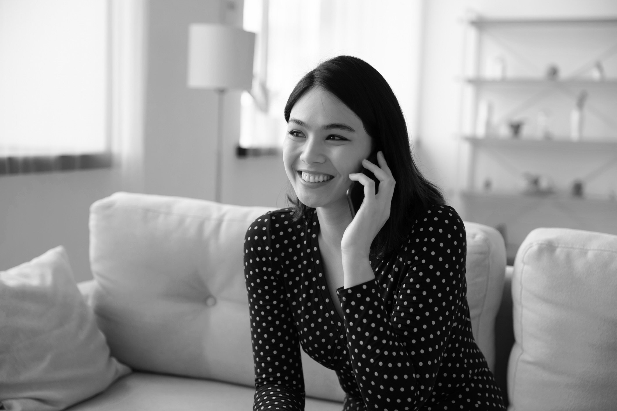 Young woman sitting on couch smiling while on the phone.